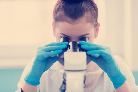 Young female student scientist looking through a microscope while doing some research in the laboratory