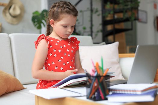 Little girl sits at the desl at home and does homework, self study of the material, reading book. The concept of distance education