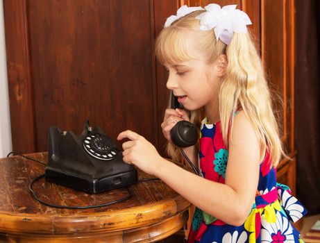 Adorable little blonde girl put your ear to the handset of the old phone. retro style