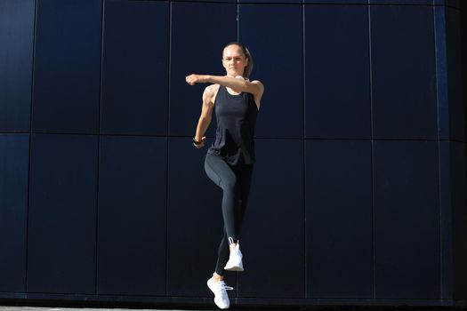 Photo of modern athletic woman in sports clothing jumping while exercising outdoors