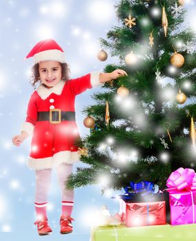 Smiling curly-haired little girl, dressed as Santa Claus decorates a Christmas tree toys.Blue winter background with white snowflakes.