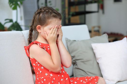 Sad little girl sitting on sofa alone at home