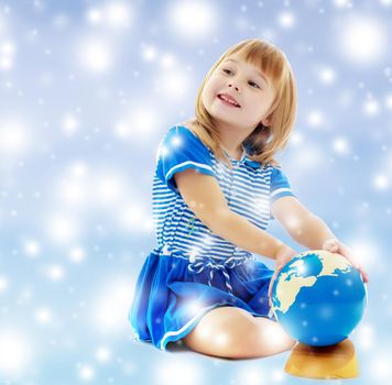 On a blue background with white blurry circles, like Christmas snowflakes. Nice little girl in a Sea blue dress sitting on the floor. Girl turns hand the globe.