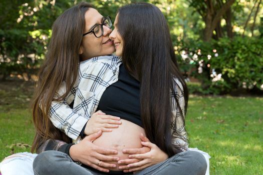 Portrait of affectionate pregnant lesbian couple relaxed at the park. Two happy girlfriends. Homosexual relationship. LGBT Community Pride. High quality photo