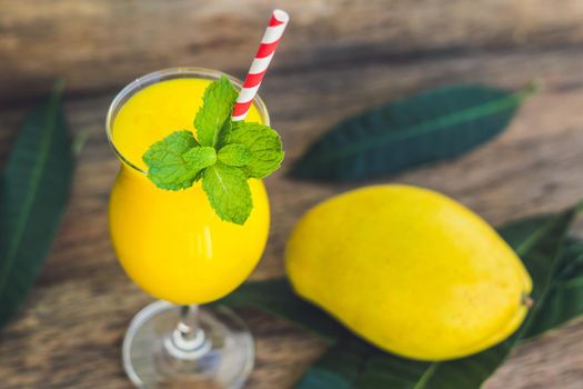 Juicy smoothie from mango in glass with striped red straw and with a mint leaf on old wooden background. Healthy life concept, copy space.