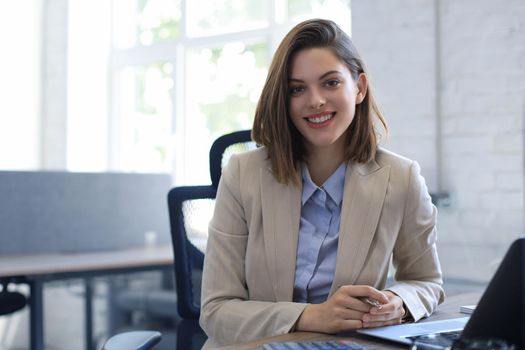 Attractive cheerful business woman working on laptop at modern office