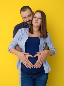 Portrait of a happy young couple,man holding his pregnant wife belly isolated over yellow background