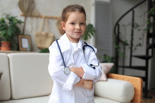 Smiling little girl in medical uniform playing with stethoscope at home