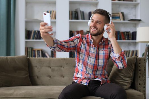 Attractive man taking selfie photo or self video with mobile phone at home sitting on couch