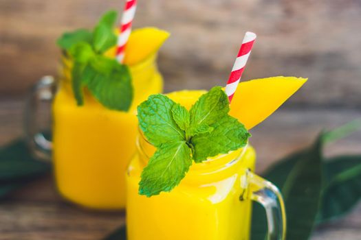 Juicy smoothie from mango in two glass mason jars with striped red straw on old wooden background. Healthy life concept, copy space.