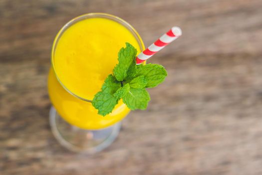 Juicy smoothie from mango in glass with striped red straw and with a mint leaf on old wooden background. Healthy life concept, copy space.