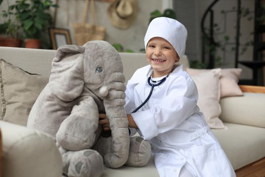 Adorable child dressed as doctor playing with toy elephant, checking its breath with stethoscope