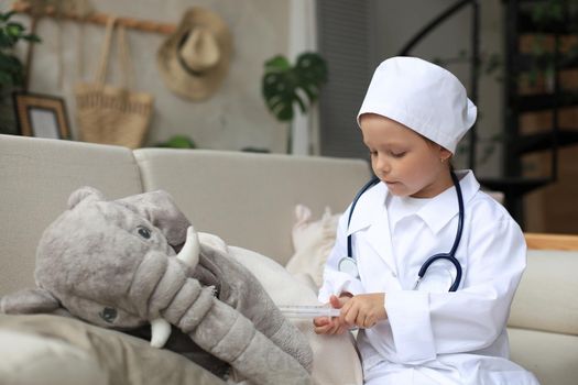 Adorable child dressed as doctor playing with toy elephant, checking its breath with stethoscope