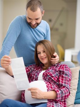 Young pregnant couple looking baby's ultrasound photo while relaxing on sofa at home