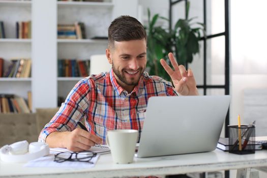 Smiling businessman greeting colleagues in video conference and negotiating distantly from home