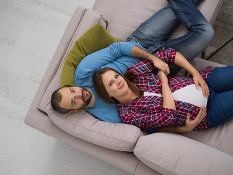 top view of happy pregnant couple relaxing on sofa couch at home