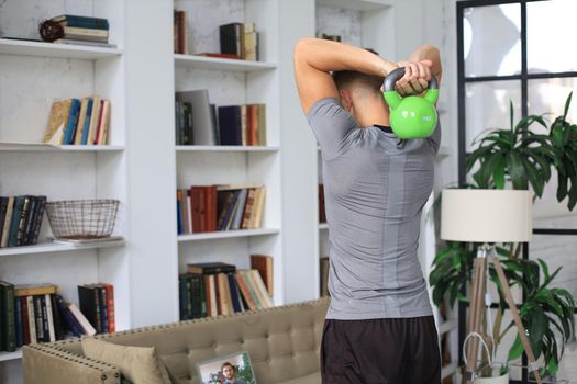 Handsome man doing sport exercise with kettlebell at home. Concept of healthy life