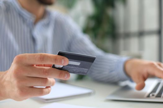 Young man sitting in office and pays by credit card with his tablet