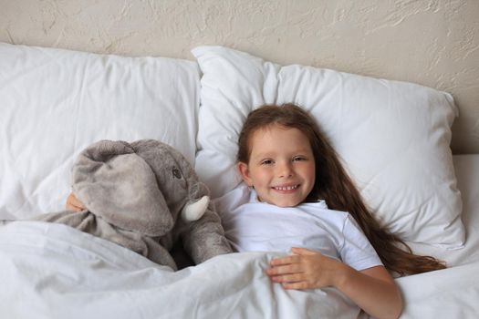 Cute child little girl wake up and lies in the bed with a toy elephant