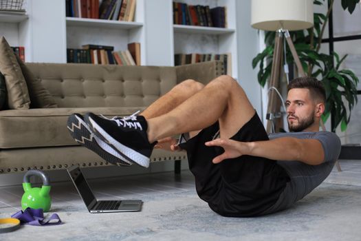 Handsome man doing abs exercises at home during quarantine. Concept of healthy life