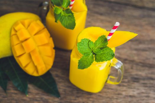 Juicy smoothie from mango in two glass mason jars with striped red straw on old wooden background. Healthy life concept, copy space.