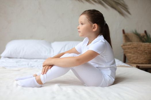 Sweet little girl sitting on her bed at home