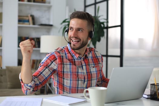 Handsome businessman is keeping arms raised and expressing joyful at home office