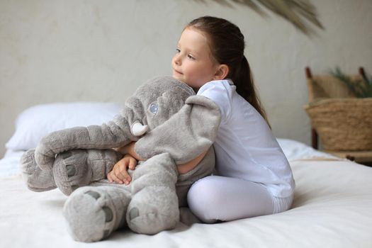 Sweet little girl sitting on her bed at home with toy elephant