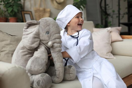 Adorable child dressed as doctor playing with toy elephant, checking its breath with stethoscope