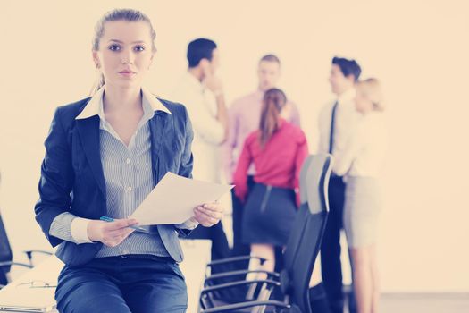 Successful business woman standing with her staff in background at modern bright office