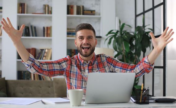 Handsome businessman is keeping arms raised and expressing joyful at home office