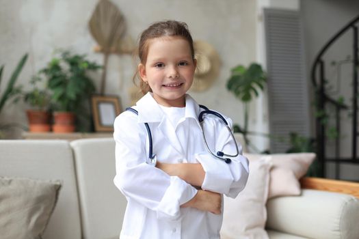 Smiling little girl in medical uniform playing with stethoscope at home