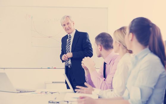 Senior male business man giving a presentation at a  meeting at modern light office on a table board