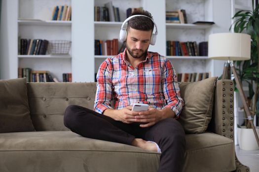 Attractive young man relaxing on a couch at home and using mobile phone for cheking social nets