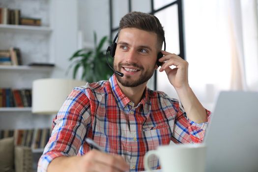 Happy young man in earphones working on laptop from home during self isolation