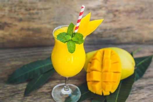 Juicy smoothie from mango in glass with striped red straw and with a mint leaf on old wooden background. Healthy life concept, copy space.