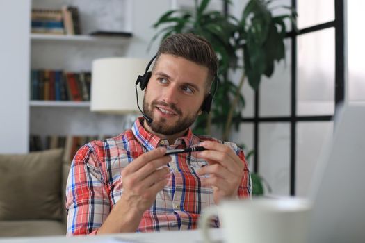 Happy young man in earphones working on laptop from home during self isolation