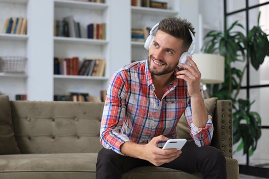 Attractive young man relaxing on a couch at home and using mobile phone for cheking social nets