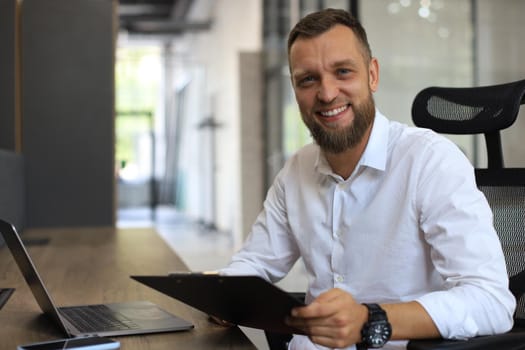 Young man is working with papers while sitting in the office. Successful entrepreneur is studying documents with attentive and concentrated look.