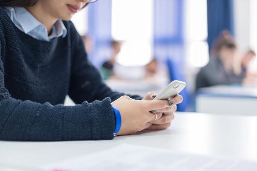 young female student using a mobile phone during the break in the classroom