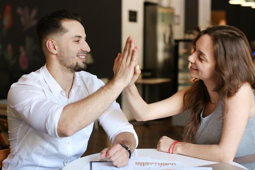 Successful businessman and woman working with documents and diagrams, giving high five. Concept of business and occupation.