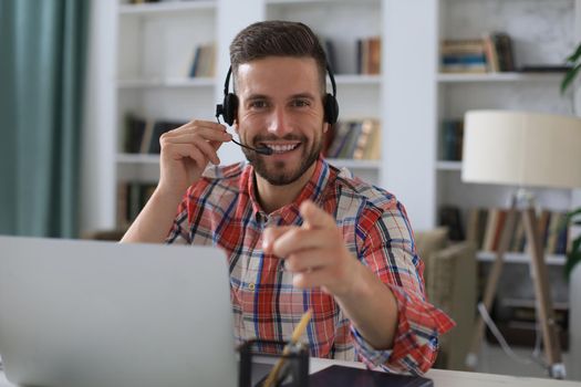 Happy young man in earphones working on laptop from home during self isolation