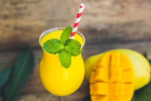 Juicy smoothie from mango in glass with striped red straw and with a mint leaf on old wooden background. Healthy life concept, copy space.