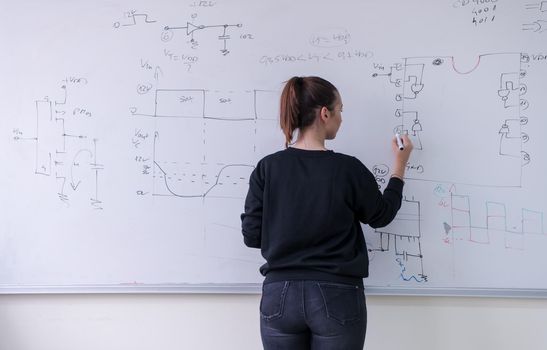 Young female student standing and writing on white chalkboard in a classroom