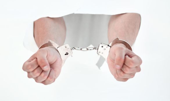 Handcuffs on the hands of a man breaking a paper wall.photo with copy space