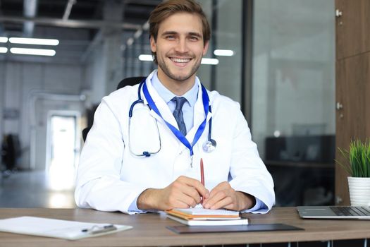 Smiling handsome male doctor talking at camera with patient