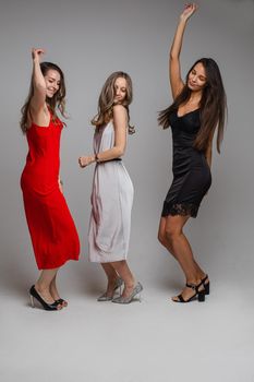 three cheerful female friends in beautiful dresses, isolated on white background