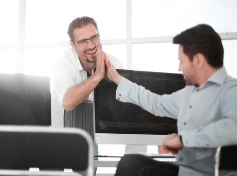 employees give each other a high five over the computer Desk. success concept