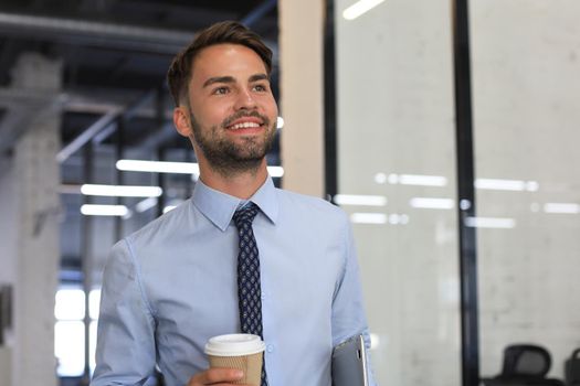 Businessman walking in office corridor with takeaway coffee