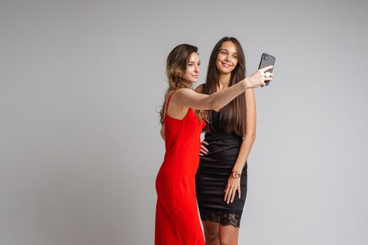 Pretty young girls bloggers wearing stylish dresses make selfie photography using phone posing on gray studio background. High quality photo